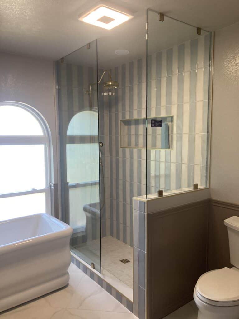 Beautiful renovated bathroom featuring a sleek glass shower, elegant tiles, and a cozy tub.