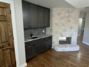 Modern kitchen with gray cabinets and stone fireplace.