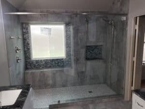 Luxury gray tile shower with dual heads, glass enclosure, and custom niche for a bathroom renovation.