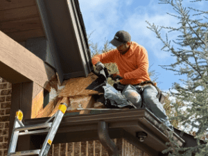 Construction worker repairing exterior siding on house roof.