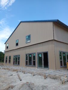 Modern house with beige siding, large windows, and steel roof under construction.