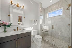 Bright, elegant bathroom with marble tiles, glass shower, and gold fixtures. Perfect for home remodeling projects.