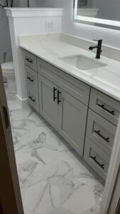 Bright modern bathroom vanity with white marble countertop and black fixtures, featuring new cabinetry and stylish hexagon marble tile flooring.