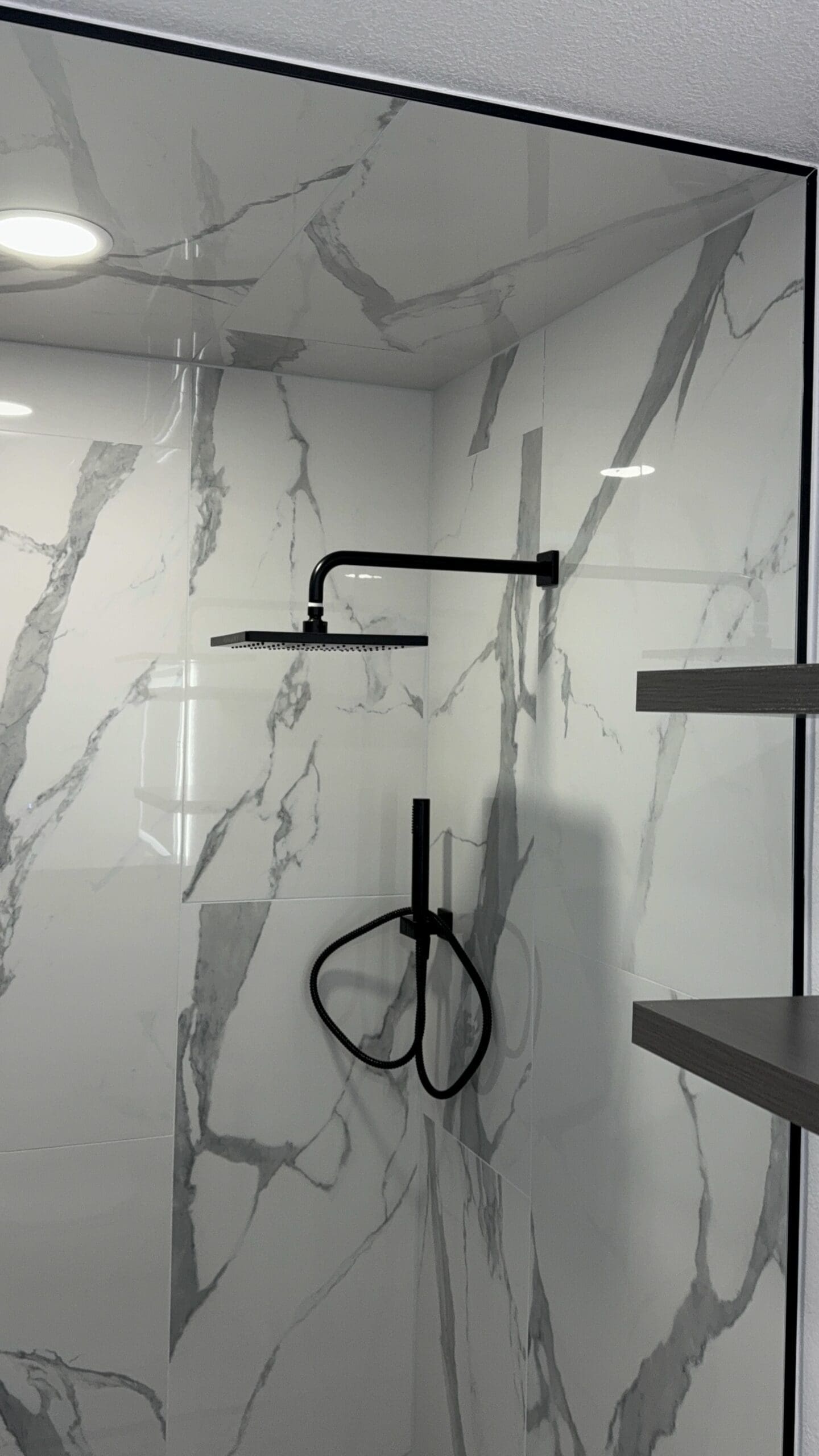 Contemporary marble tile shower with black fixtures and rain shower head.