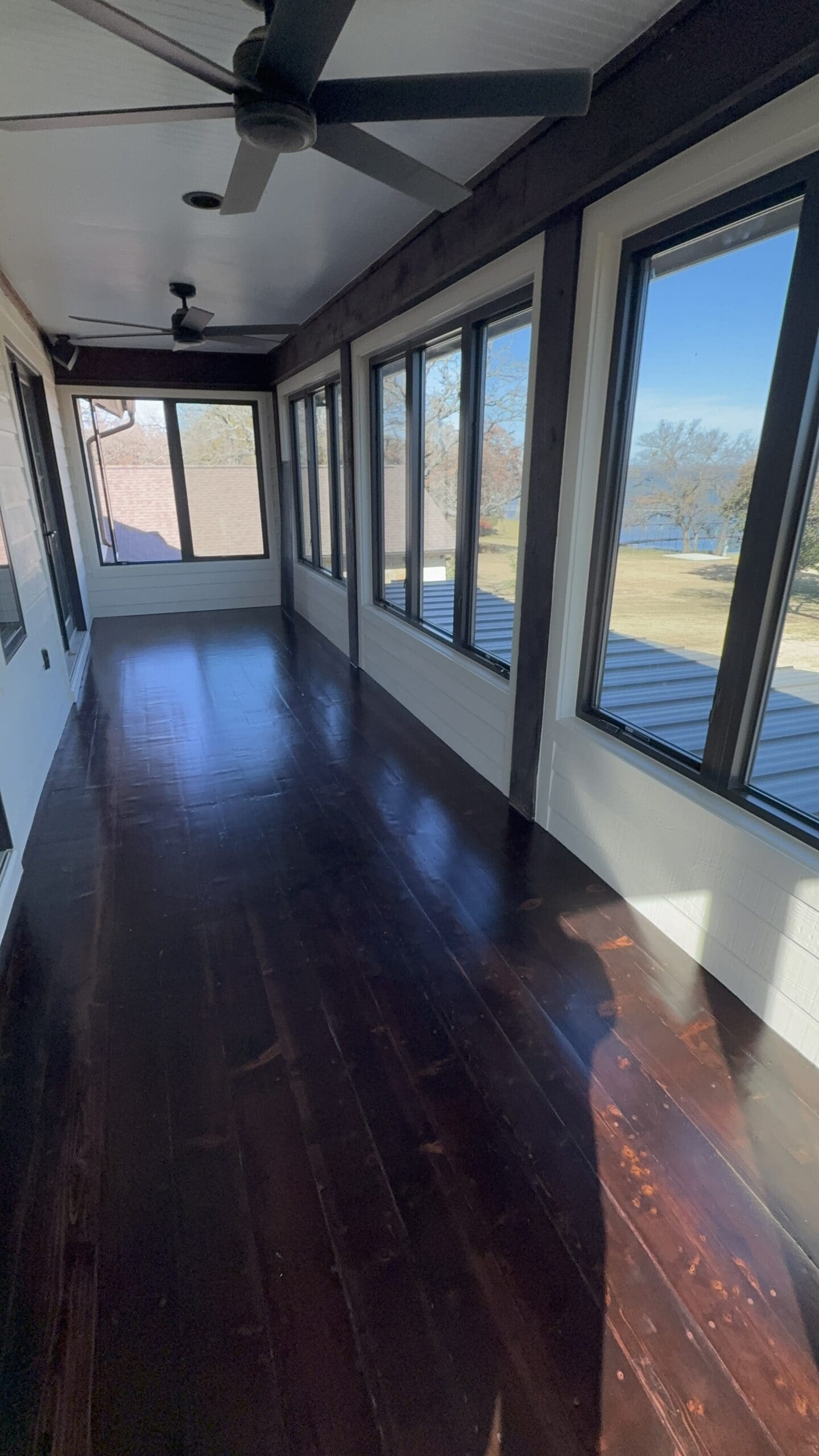 Bright modern sunroom with black wood floors, ceiling fans, and panoramic lake views.