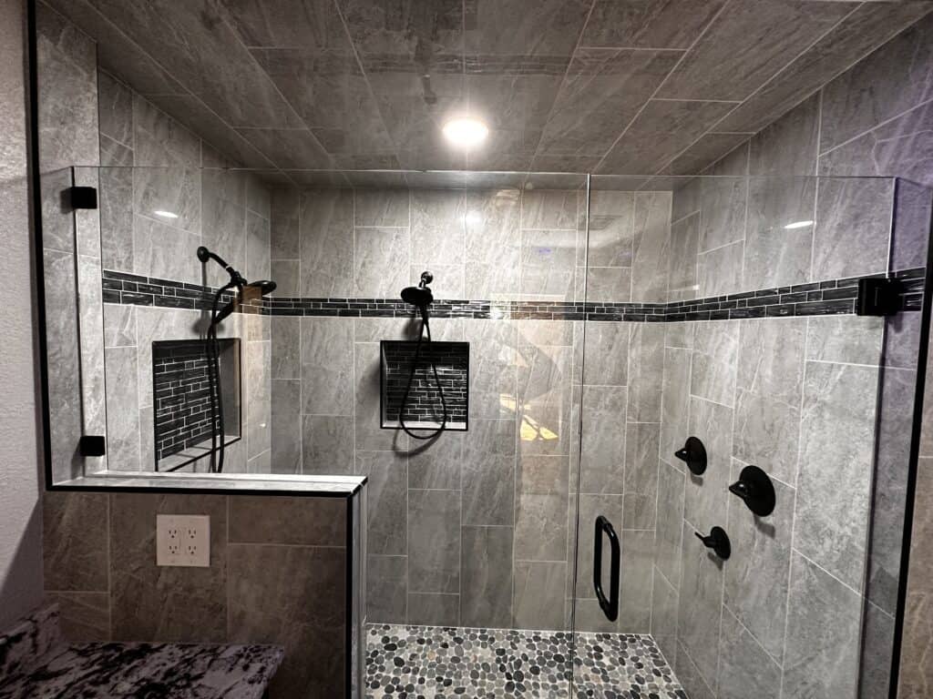 Beautiful walk-in shower with glass door, black fixtures, and sleek gray tile design.