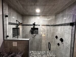 Beautiful walk-in shower with glass door, black fixtures, and sleek gray tile design.