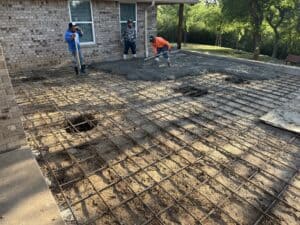Long description: Workers laying rebar and pouring concrete for a home extension or patio, focusing on durable foundation work.