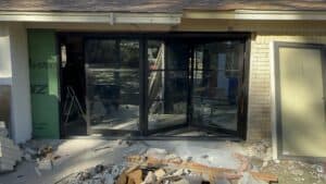 Modern black-framed glass doors under construction with debris and building materials around.
