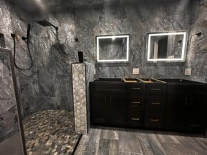 Luxurious bathroom with marble walls, black cabinetry, and illuminated mirrors for a sleek, upscale look.
