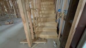 Bright, unfinished interior showcasing new wooden staircase structure under construction.