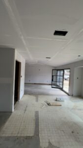 Bright, open space with drywall installation, ceiling work, and unfinished flooring.