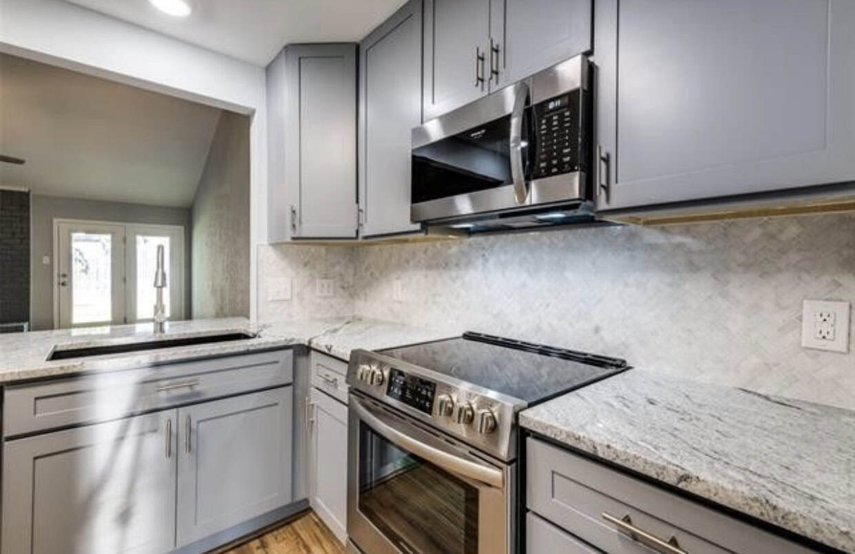 Contemporary kitchen with gray cabinets, stainless steel appliances, and marble countertops.