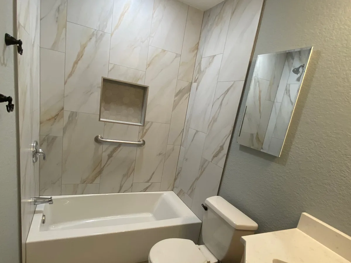 Tub with calacatta-look tile surround and glass mosaic niche by Salvation Home Remodeling