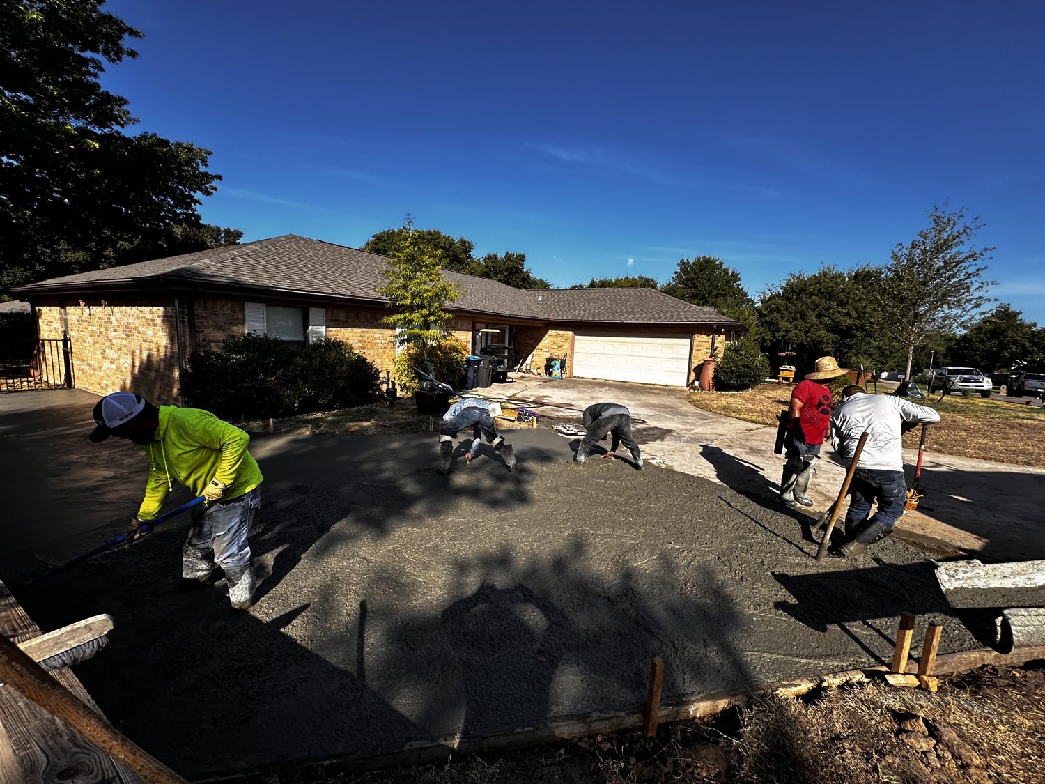 Full crew finishing a replacement concrete driveway at a Fort Worth brick ranch home.