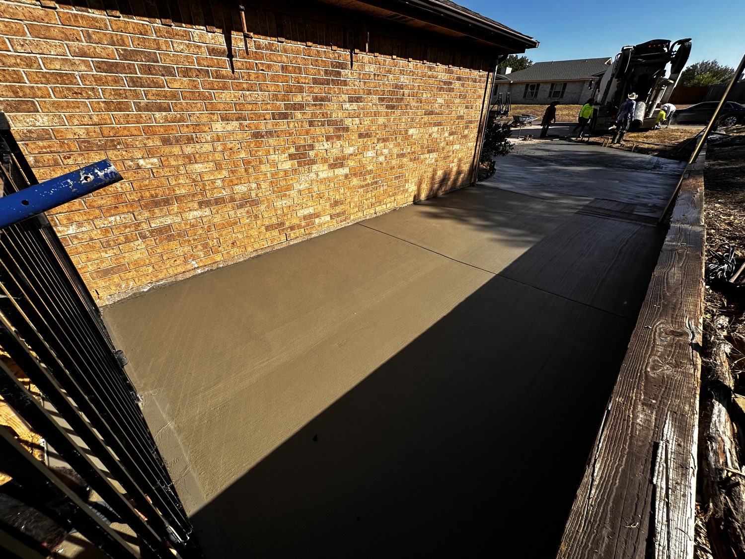 Finished concrete driveway alongside a Fort Worth brick home, forms still in place.