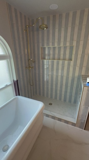 Freestanding soaking tub beside a striped tile walk-in shower with brass fixtures in a Fort Worth bathroom remodel.