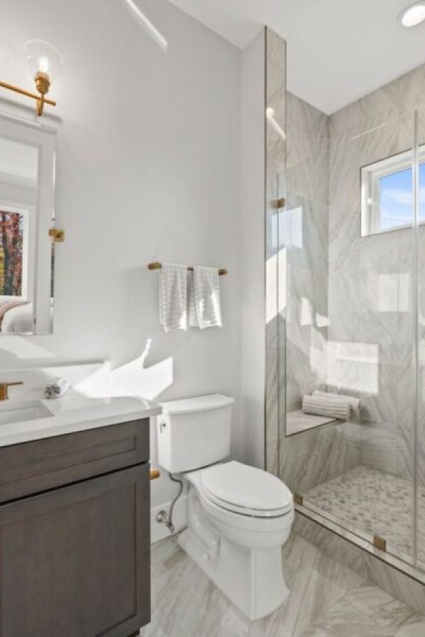 Bright, elegant bathroom with marble tiles, glass shower, and gold fixtures. Perfect for home remodeling projects.